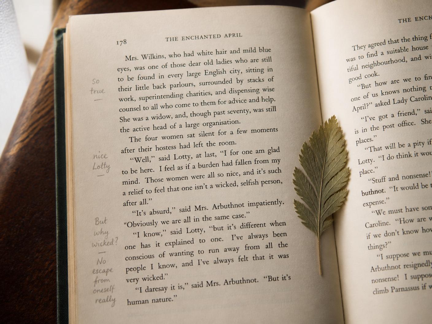 A book page with pencil marginalia and a pressed leaf between the pages.